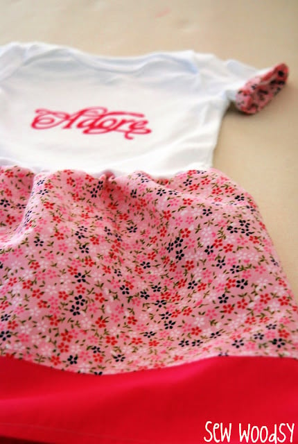 White onesie with the word "adore" on it with pink floral fabric.