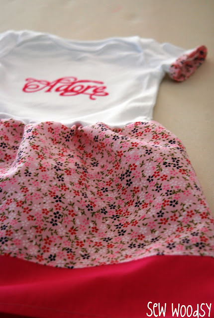 White onesie with the word "adore" on it with pink floral fabric.
