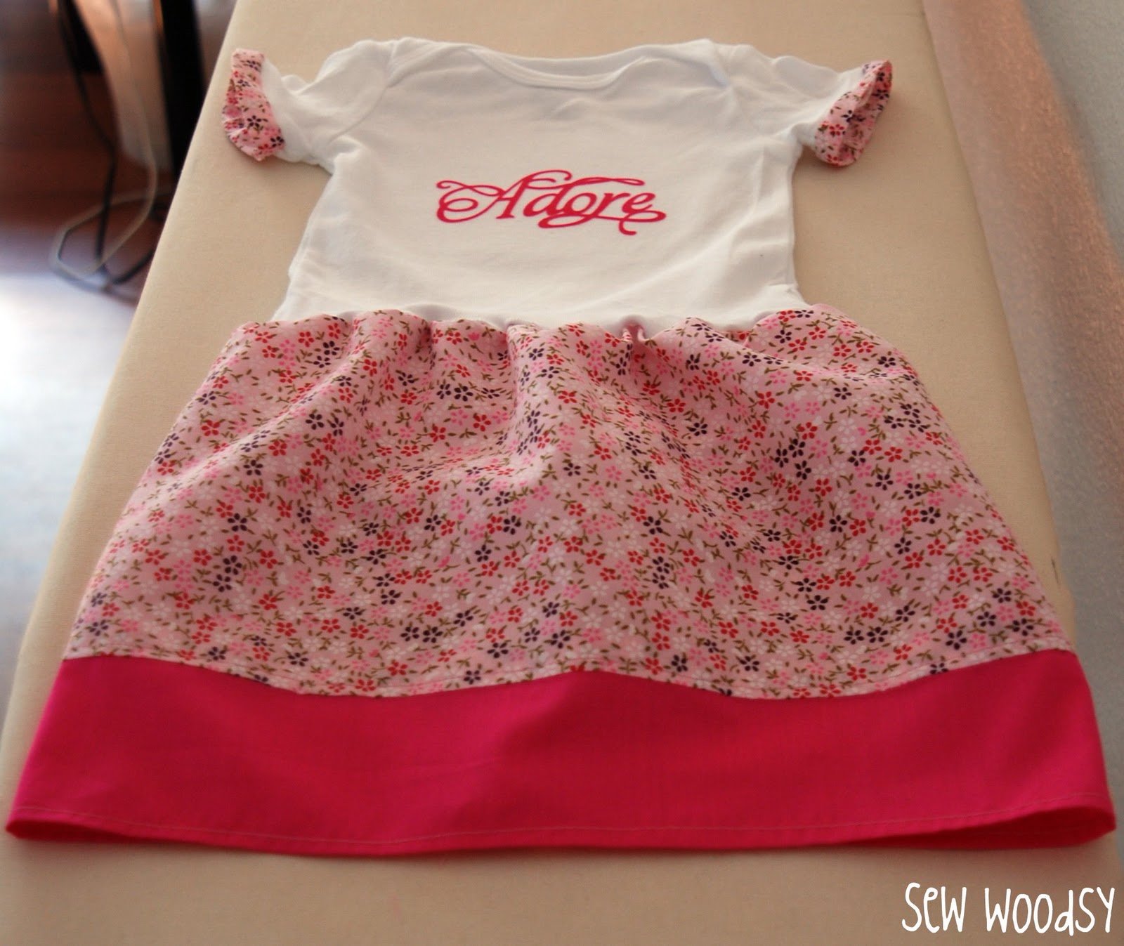 White top with flower skirt and pink trim on an ironing board.