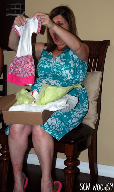 Pregnant women in shock by baby dress with an open box on lap.