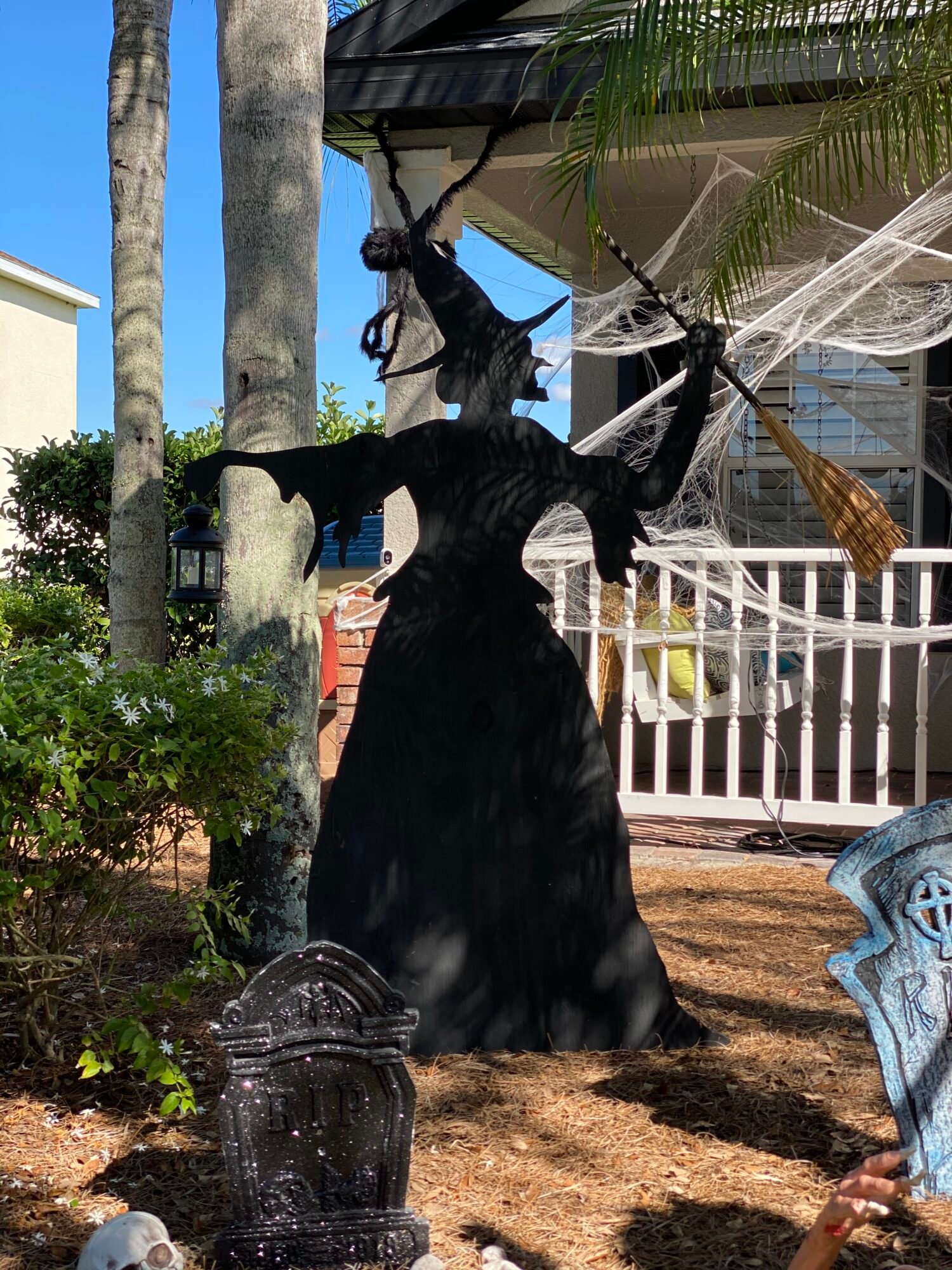 Black witch wood cut out in a yard with cob webs in the background.