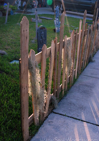 Wood pallet fence with moss hanging on it and grave stones in the background.