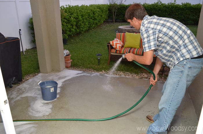 Man spraying a patio with a green hose.