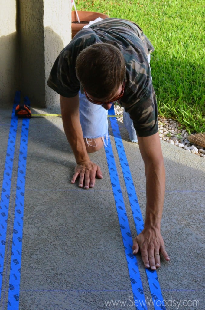 Man smoothing blue painters tape on a concrete patio.