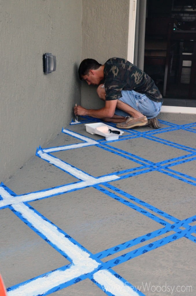 Man using a paint brush painting blue painters tape on a patio.