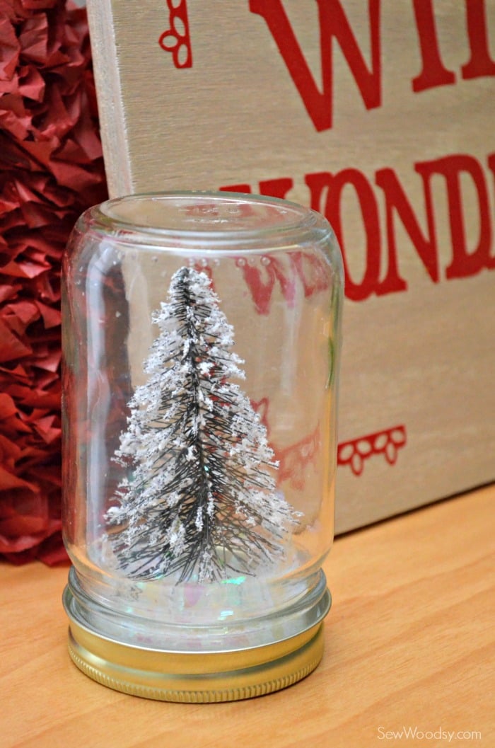 Mason jar with Christmas tree inside and fake snow on a wooden table.