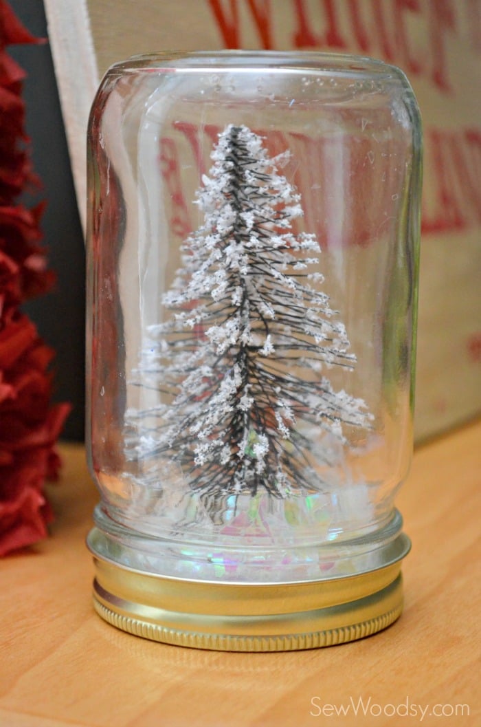 Close up of a mason jar filled with fake snow and a tree. 