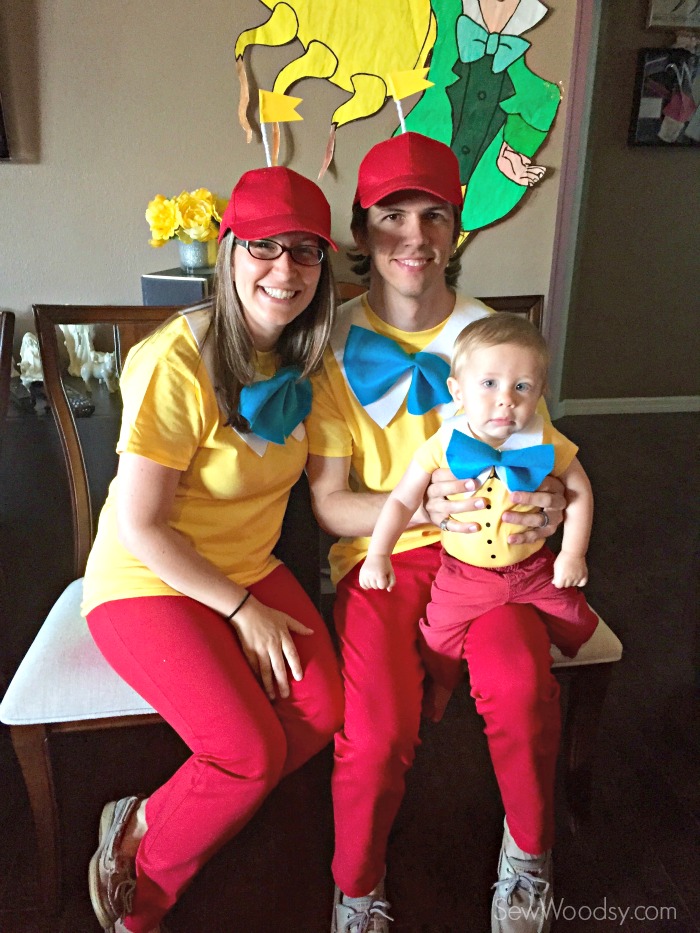 Man, woman, and baby dressed as Tweedledum and Tweedledee sitting on chairs.