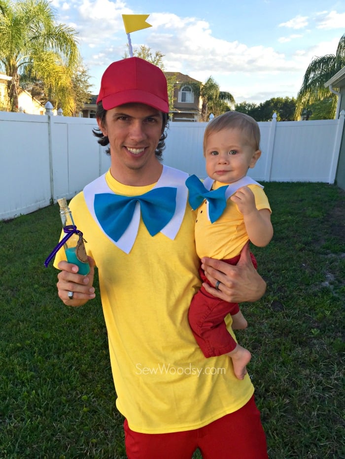 Man holding a baby, both dressed as Tweedledum and Tweedledee.