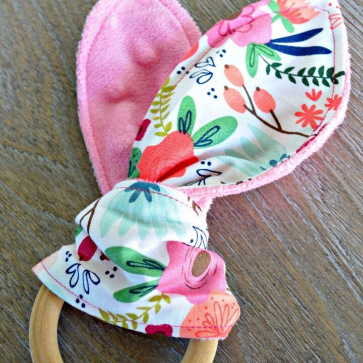 Wooden teething ring with pink and floral fabric tied around it.