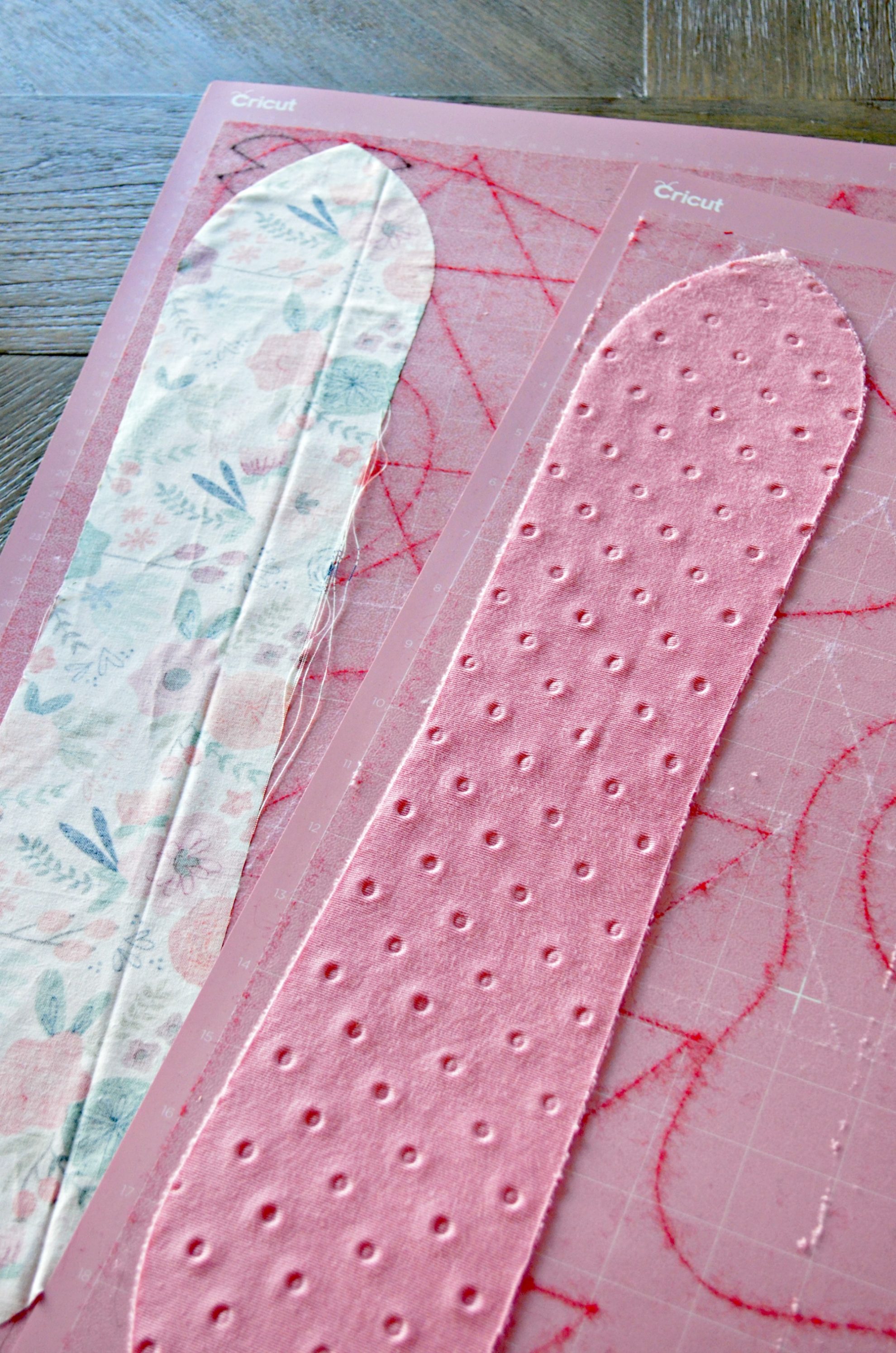 Two pink Cricut cutting mats with two pieces of cut fabric on them.