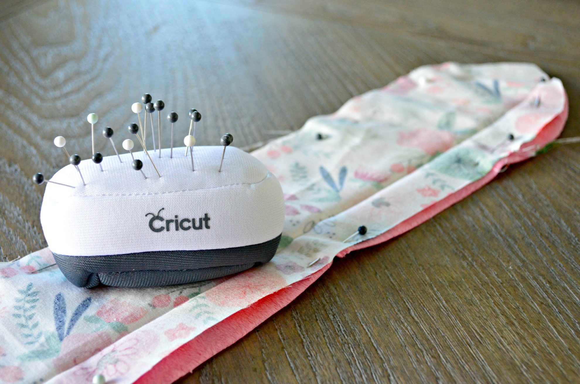 White cricut pin cushions with straight pins in them resting on top of fabric that's pinned.