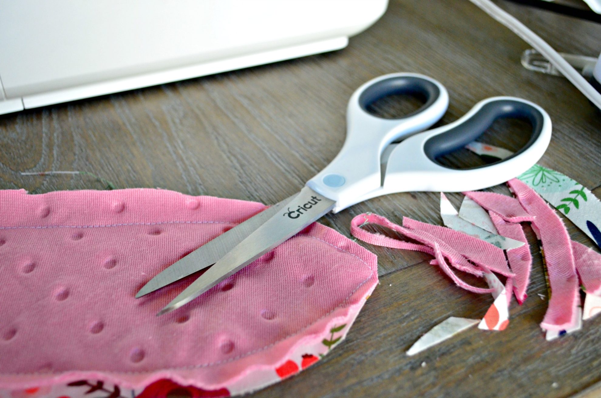 White cricut scissors on top of sewn fabric with scraps of fabric next to it.