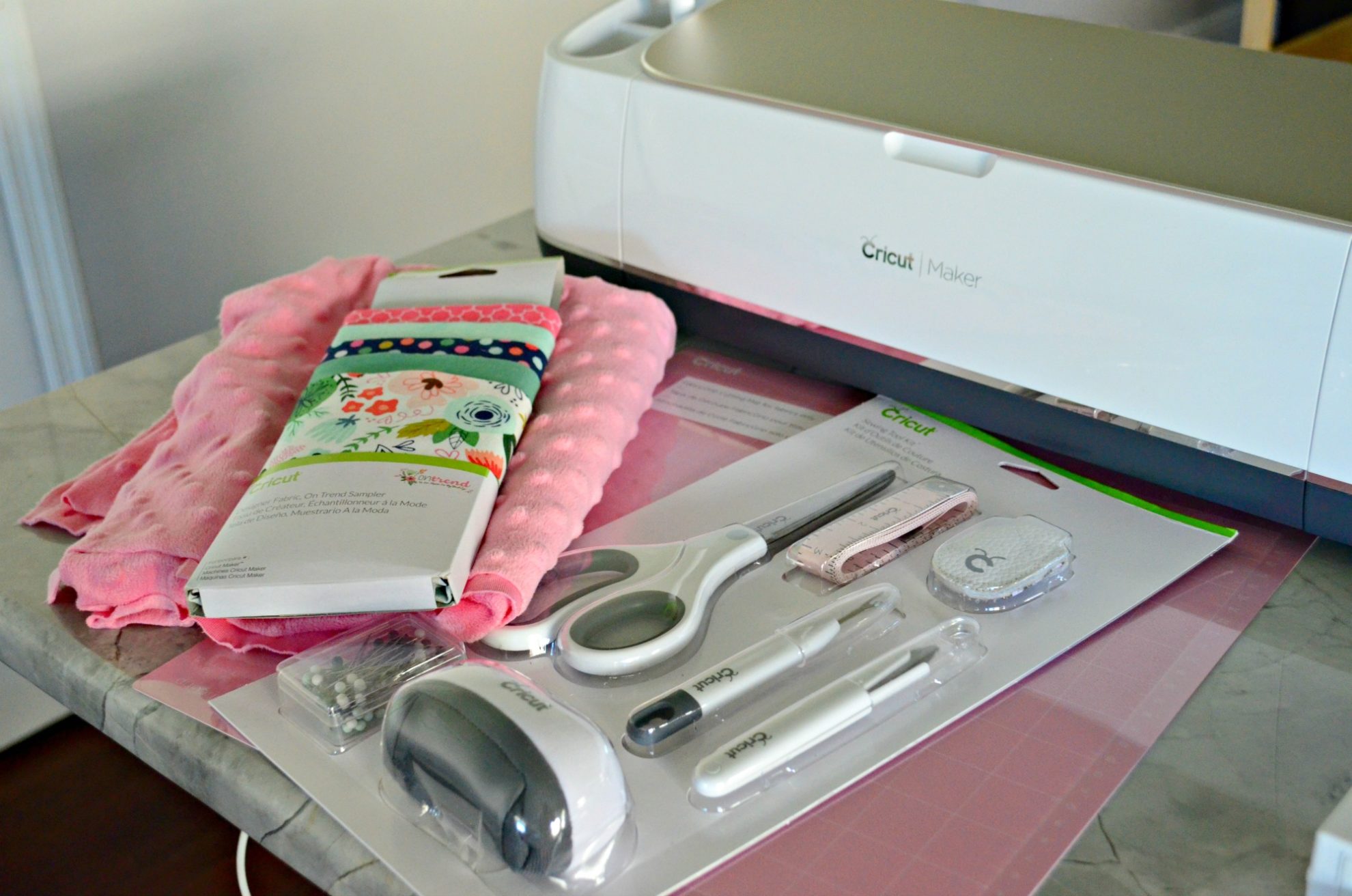 supplies on countertop: fabric, Cricut Maker, pink mat, and sewing supplies.