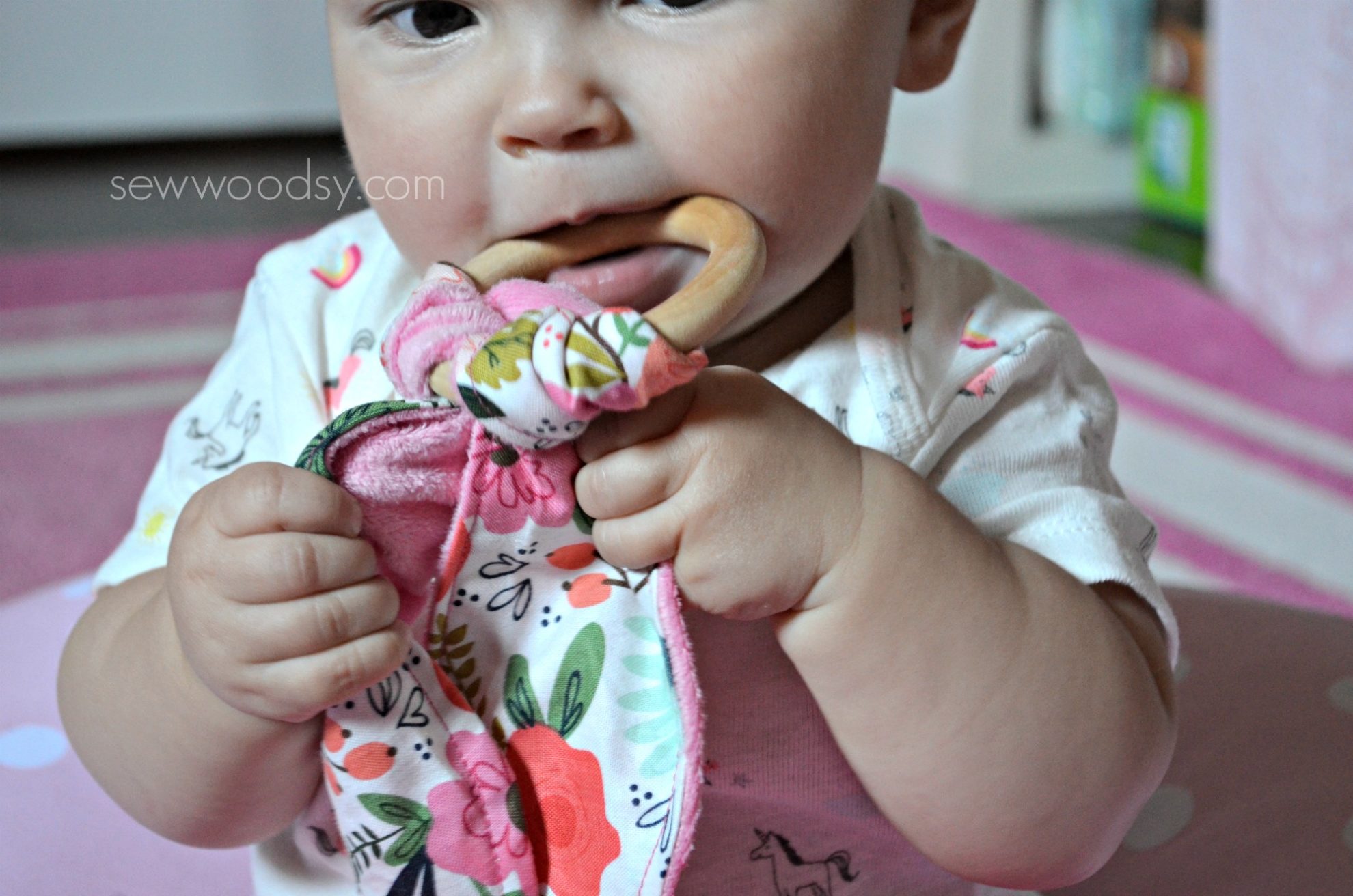 Close up of a baby girl holding a teething ring in mouth.