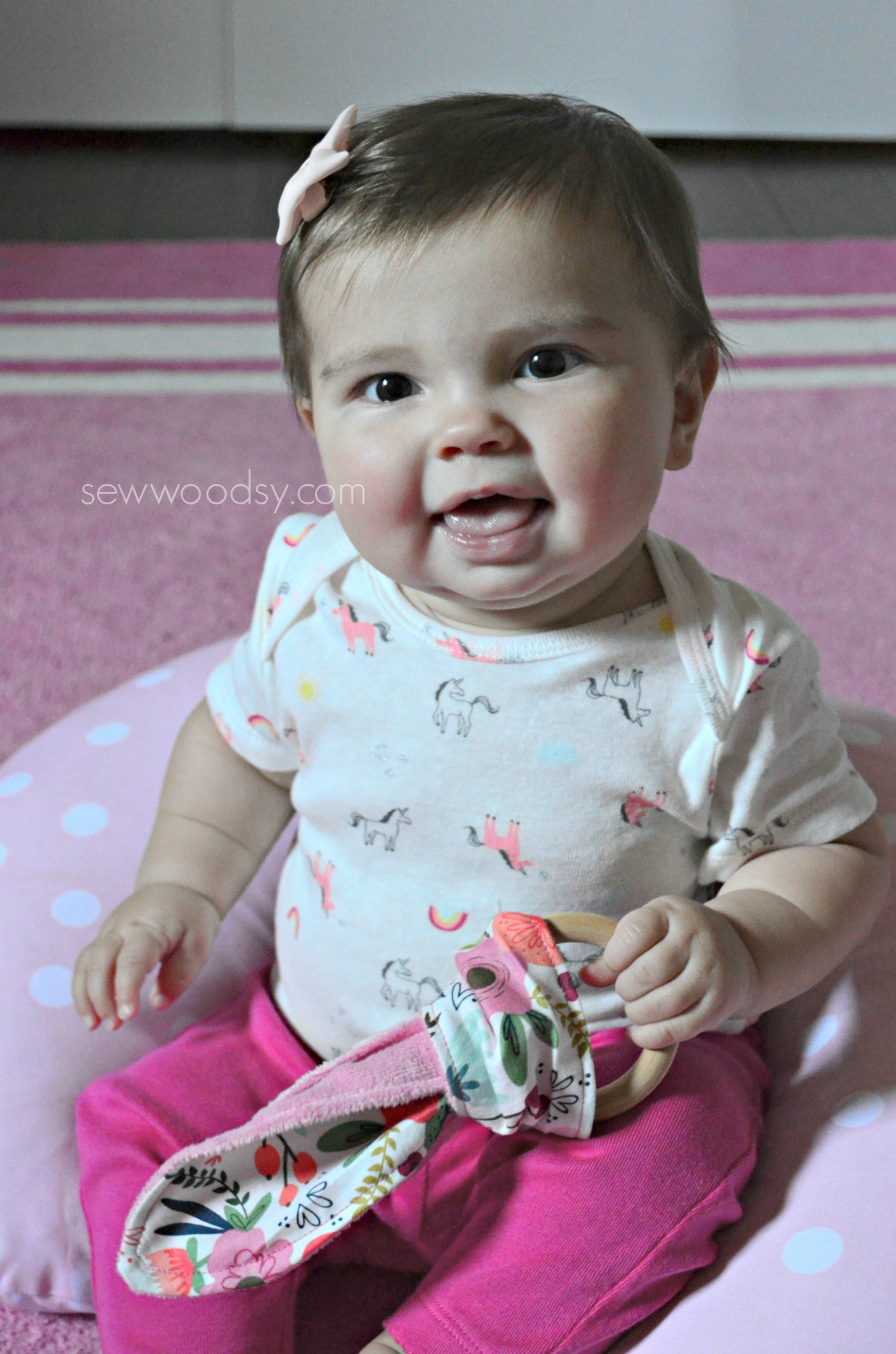 Baby girl holding a wooden teething ring with fabric.