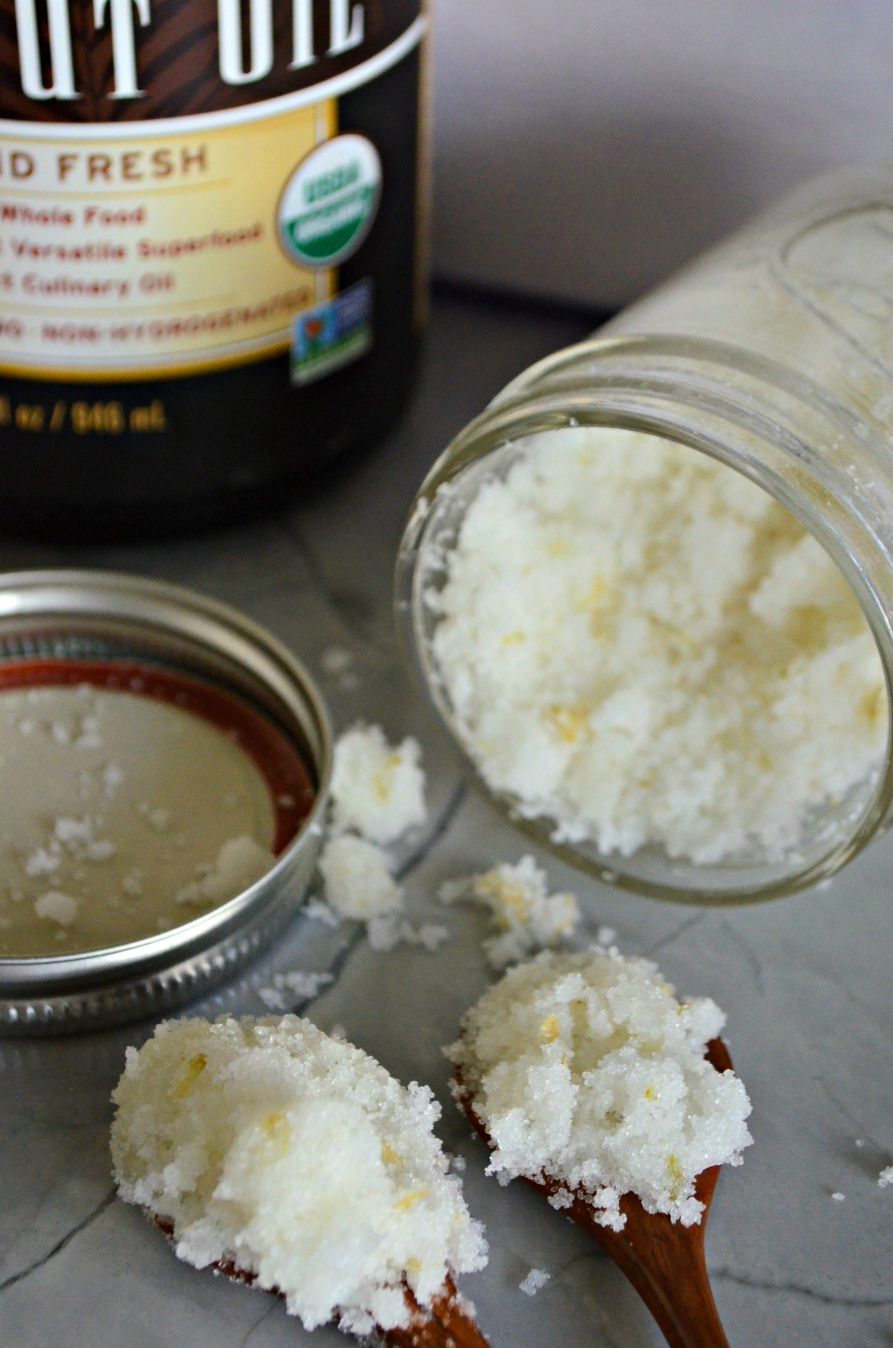 Two wooden spoons with sugar scrub on the spoons on a counter.
