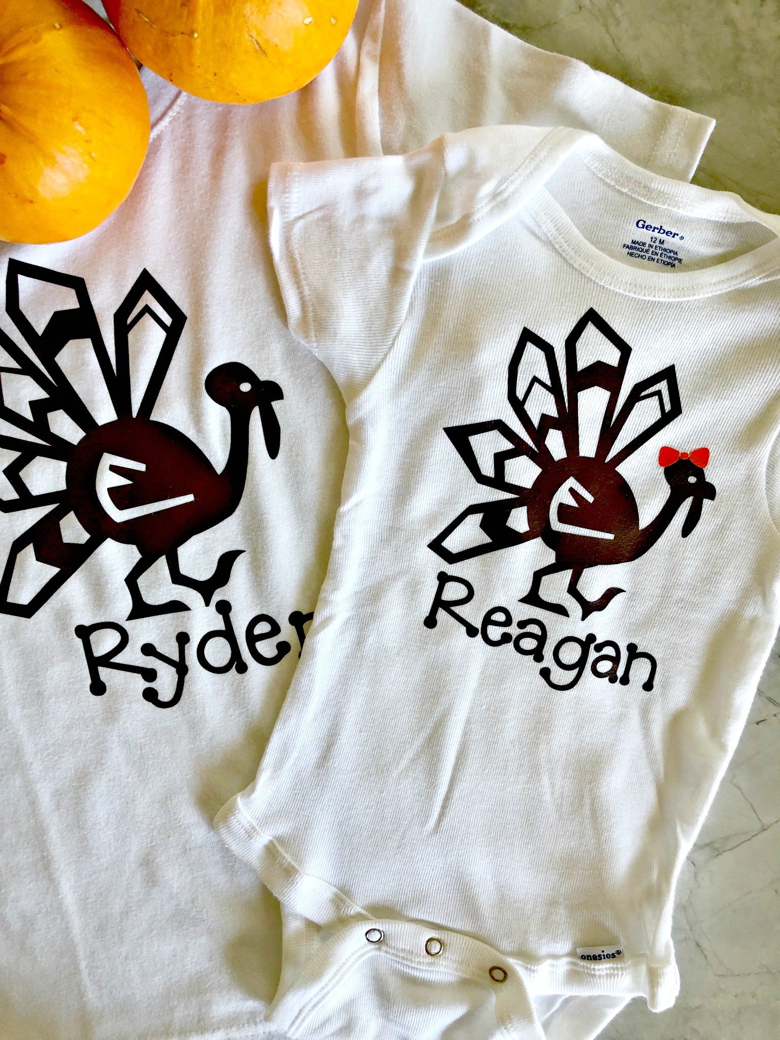 Two turkey shirts with names on them next to pumpkins.