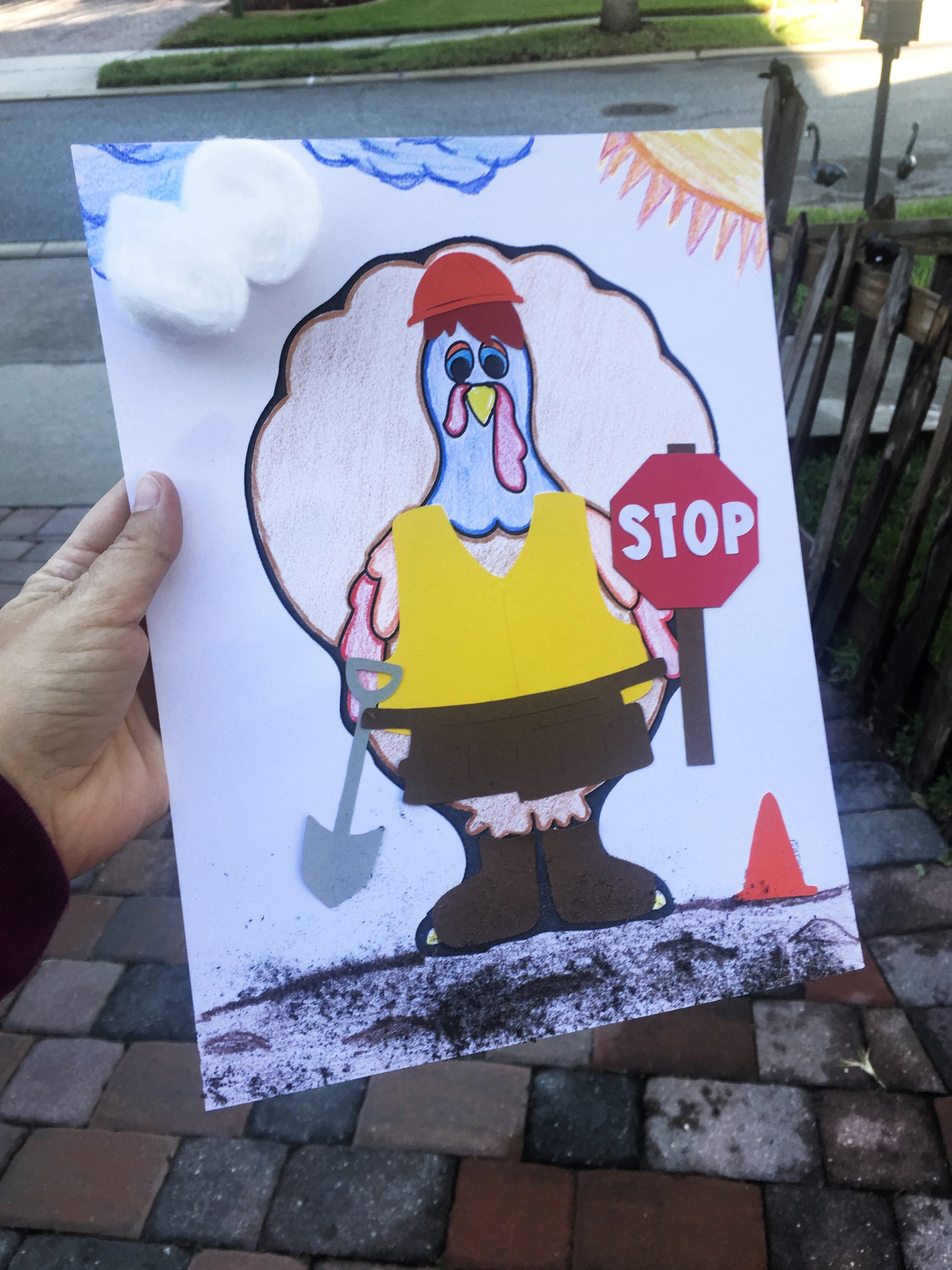 Female hand holding a paper of a Turkey In Disguise as a Construction Worker with a vest, tool belt, and stop sign with dirt on the bottom.