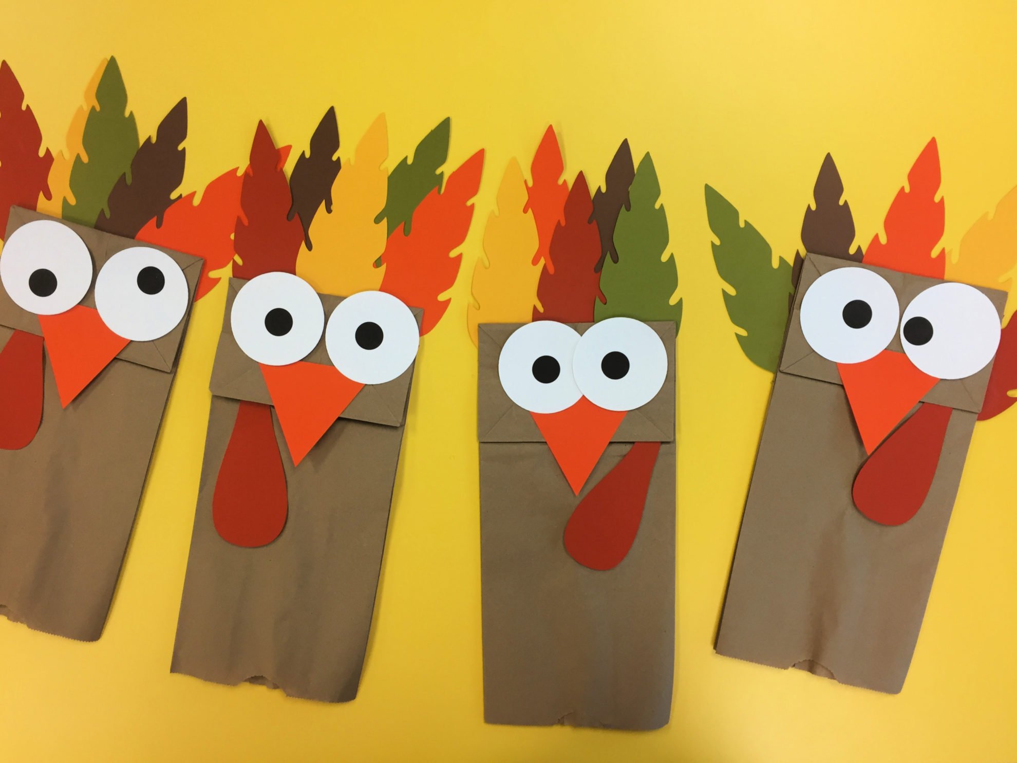 Four Turkey Paper Bag Puppets on a yellow table.