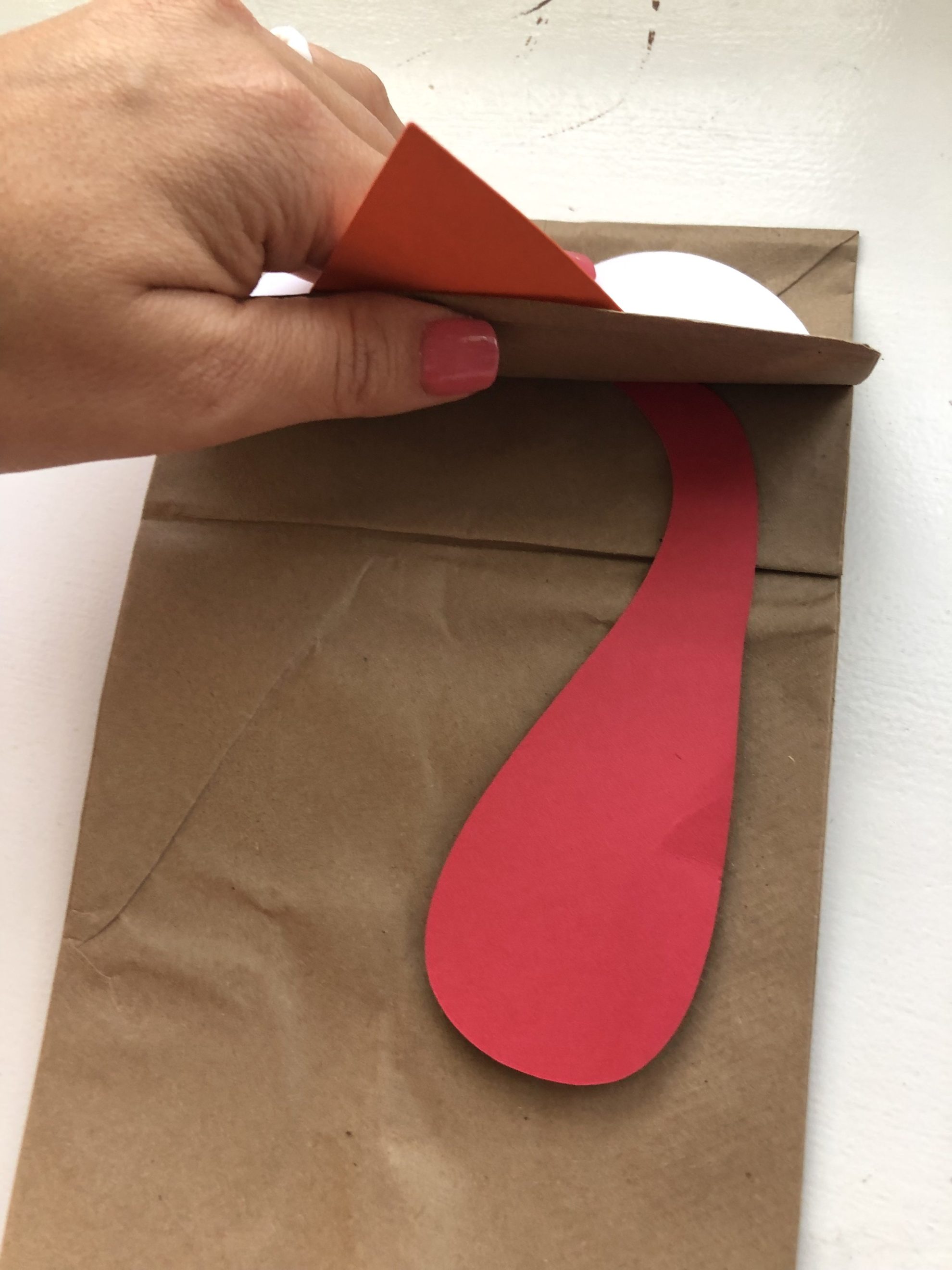 Female hand with pink nails holding a brown paper bag with a red paper gobbler tucked under the flap.