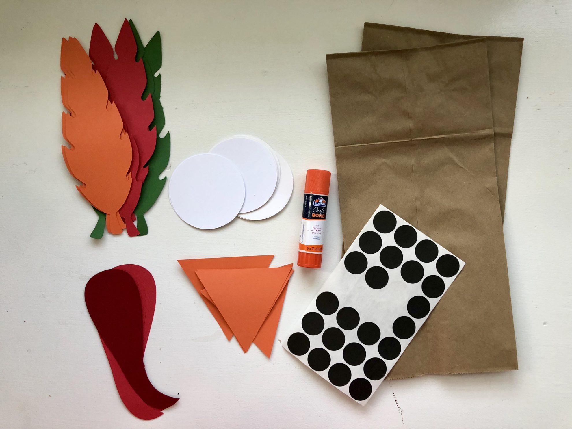 Supplies: paper feathers, white circles, orange triangles, red gobblets, glue stick, black sticker dots, and paper bags.
