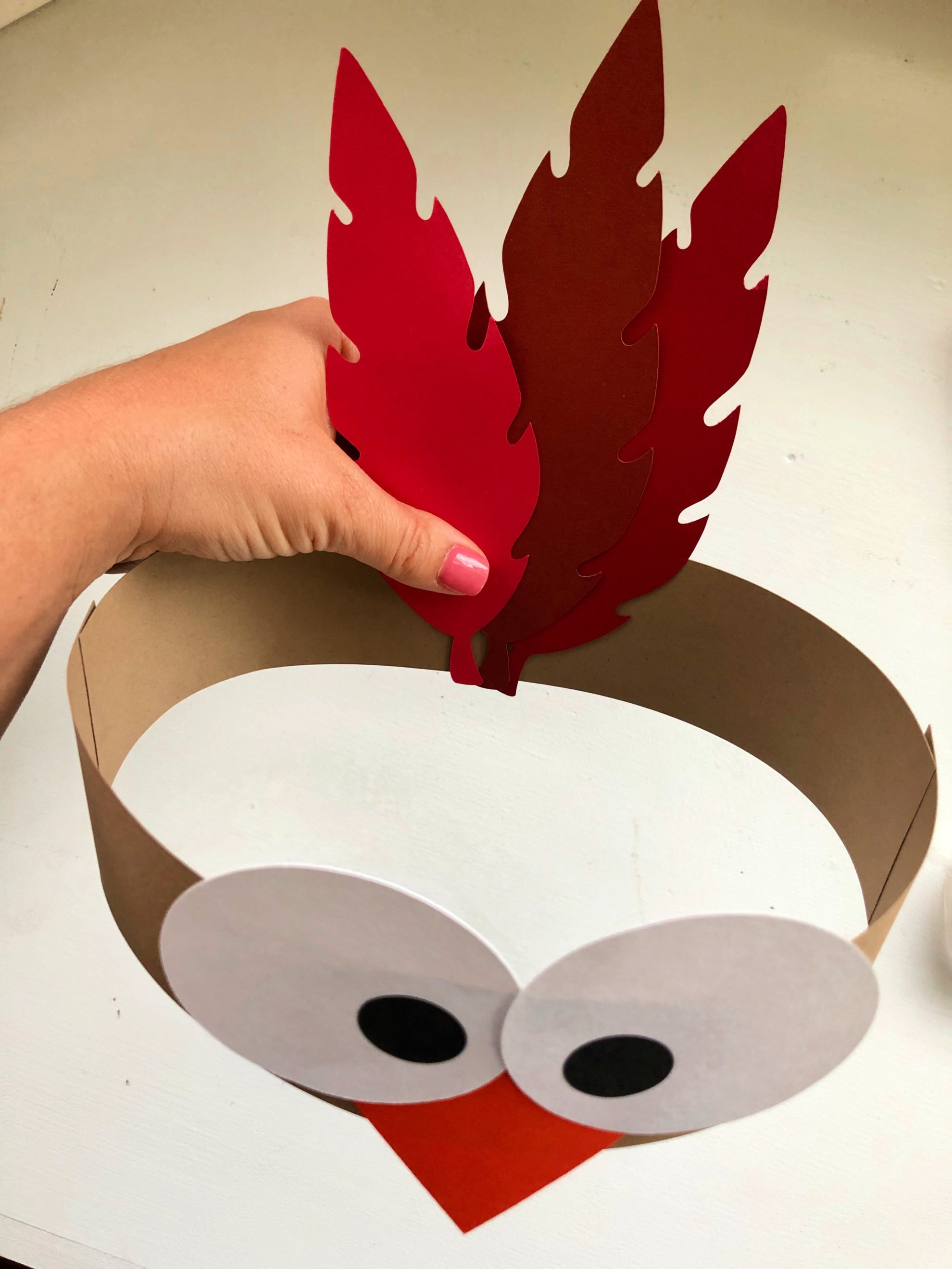 Female hand pressing paper feathers to the back of a brown paper headband.