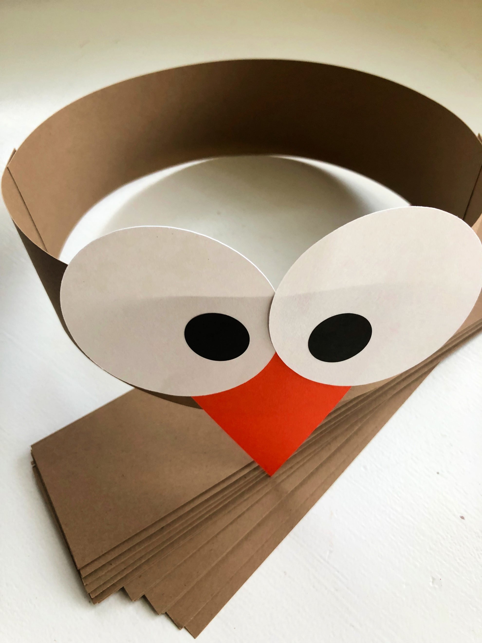 Brown paper headband with white circle and black pupil stickers with an orange triangle beak.