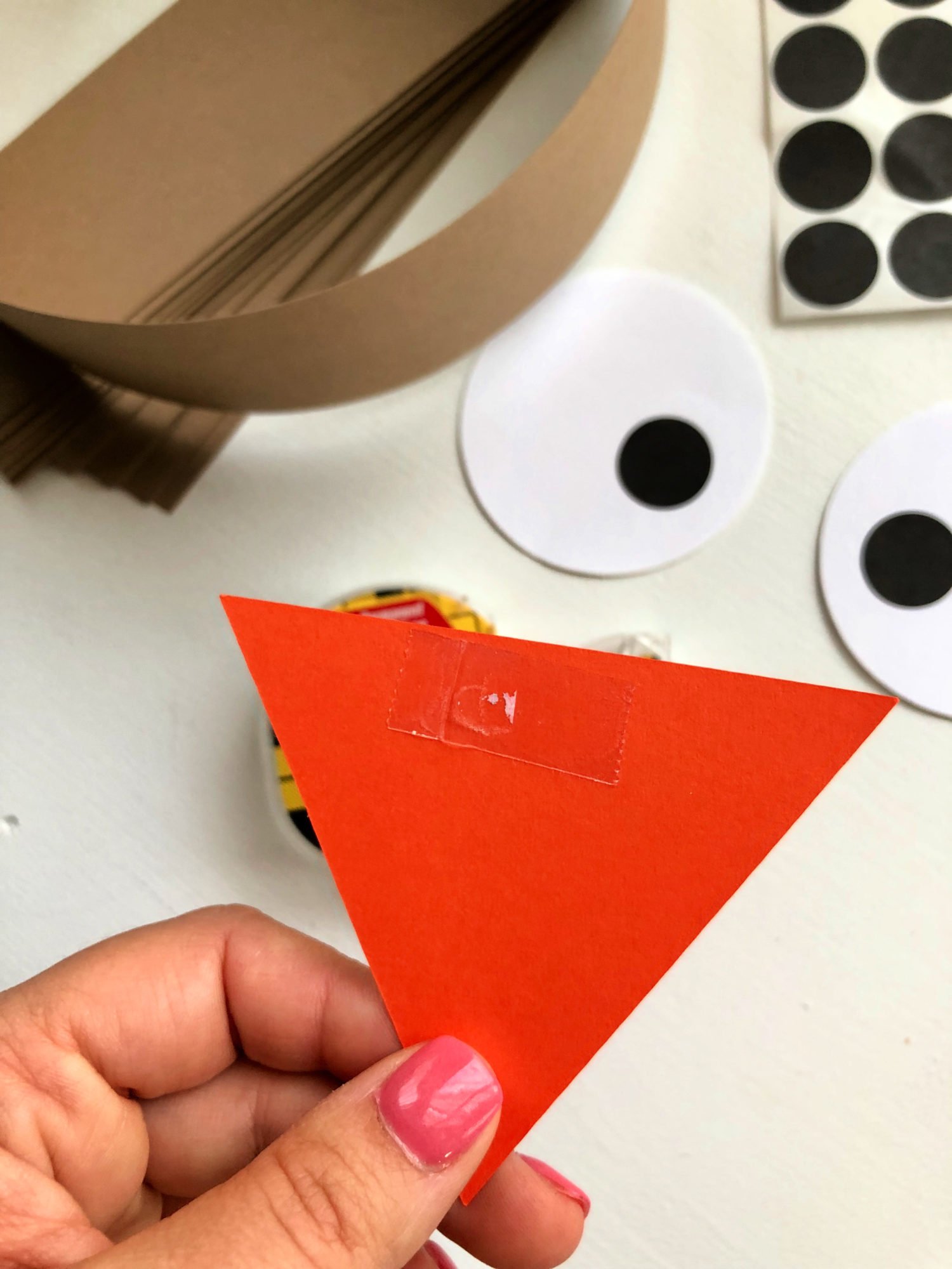 Female hand with pink nails holding an orange paper triangle.