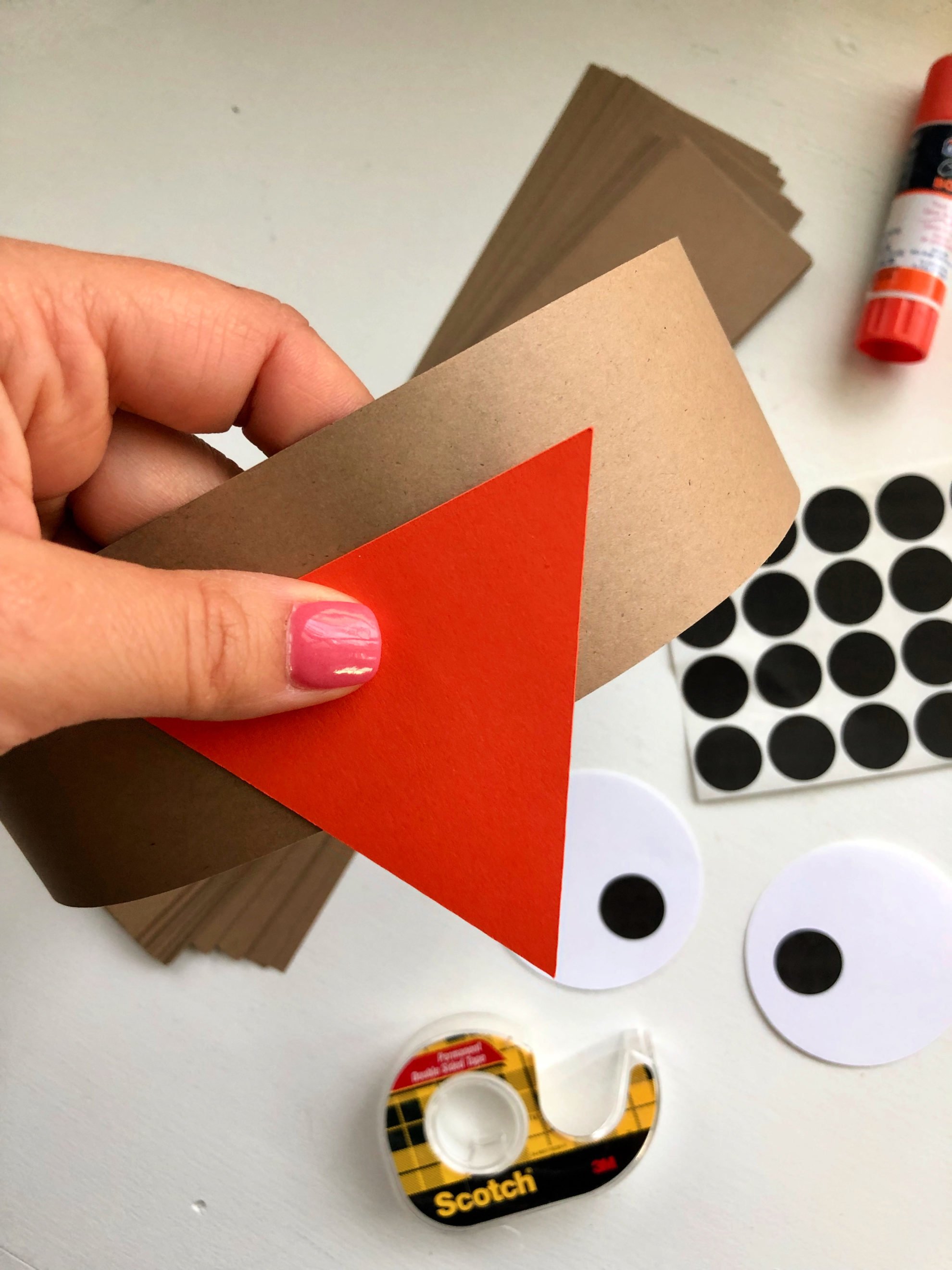 Female hand with pink nails pressing an orange triangle onto a brown circle paper band.