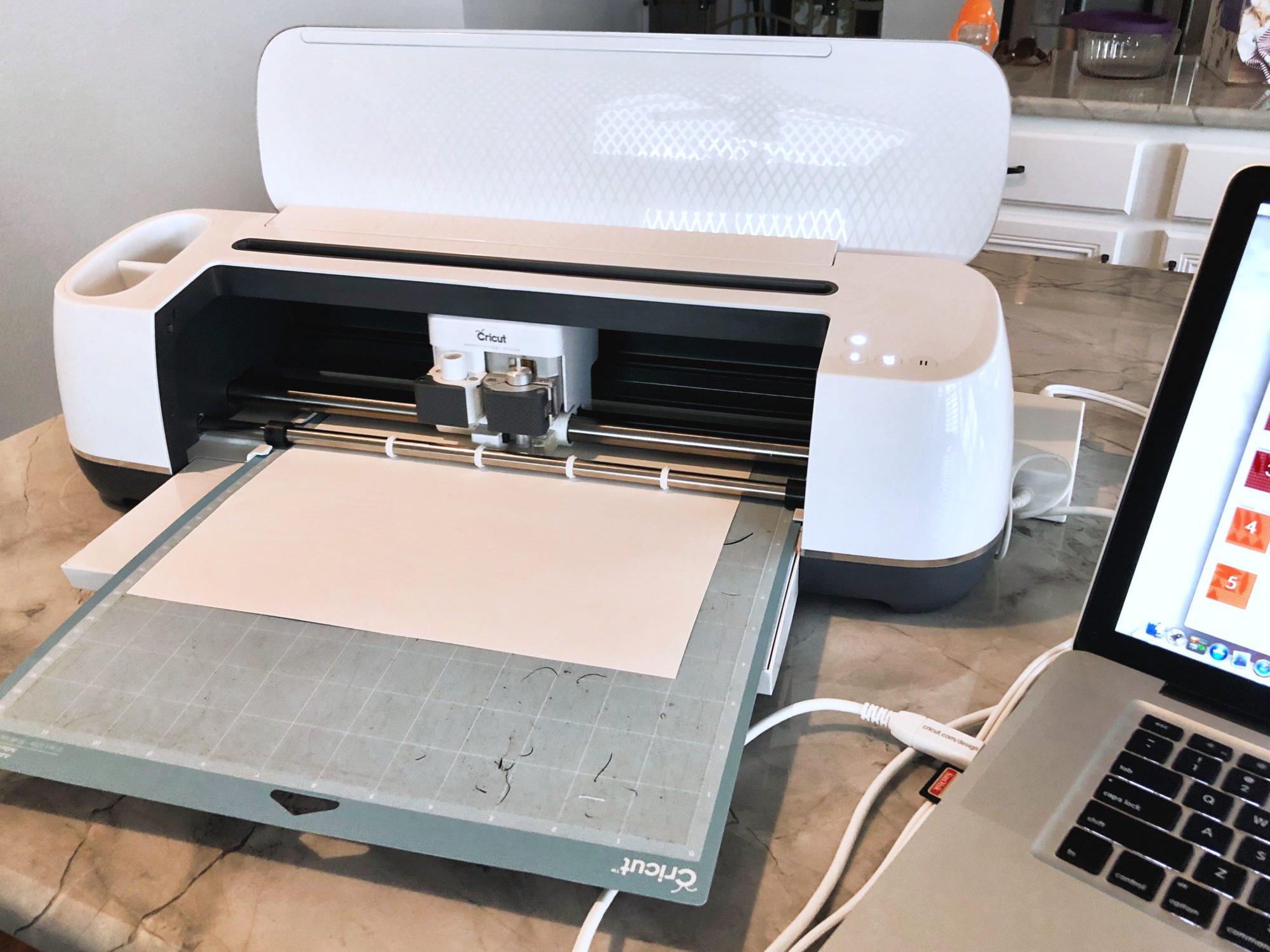 Cricut Maker loaded with white cardstock sitting on a marble countertop.