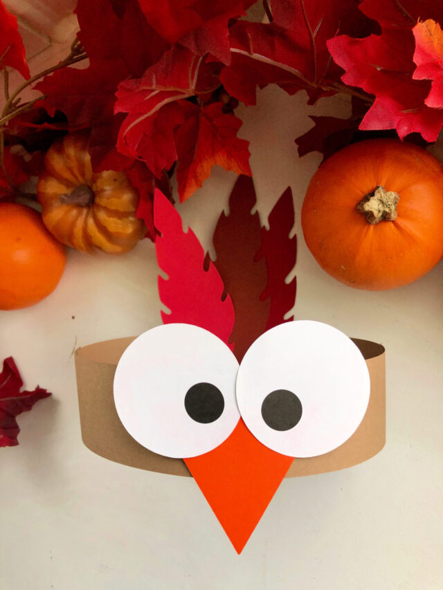 Top view of a paper turkey head band with autumn leaves.
