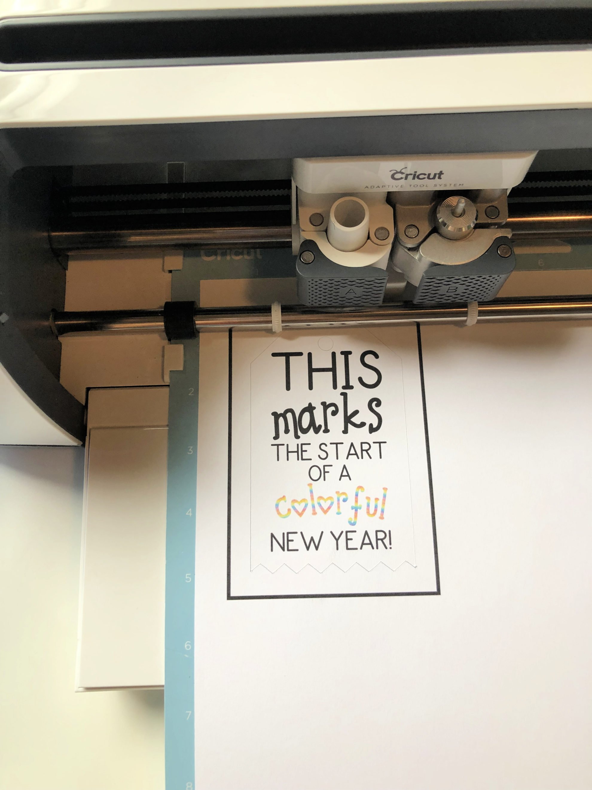 Top view of a Cricut Maker Machine cutting out a paper on a blue mat. 