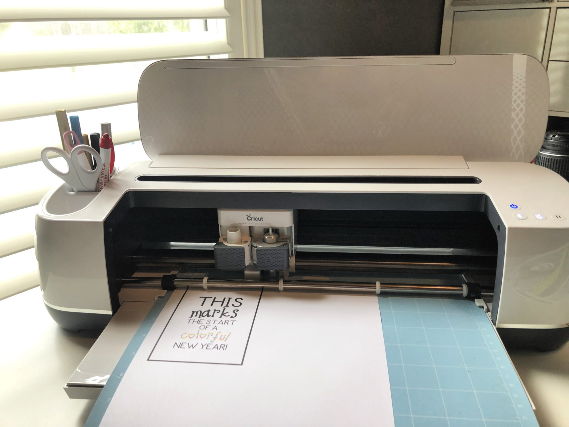 Cricut Maker with blue mat loaded and paper with printed design on paper.