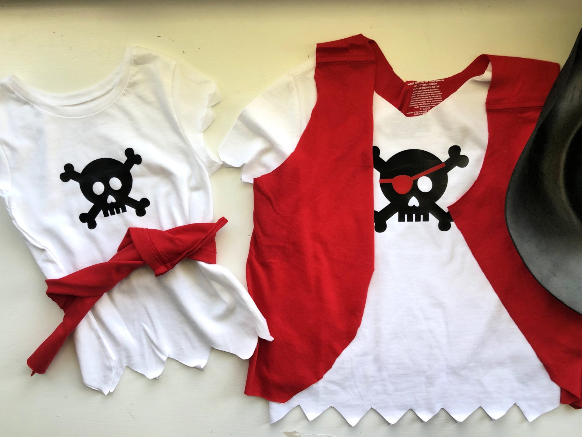 two white shirts with pirate skulls, one with a red belt and the other with a red vest. 