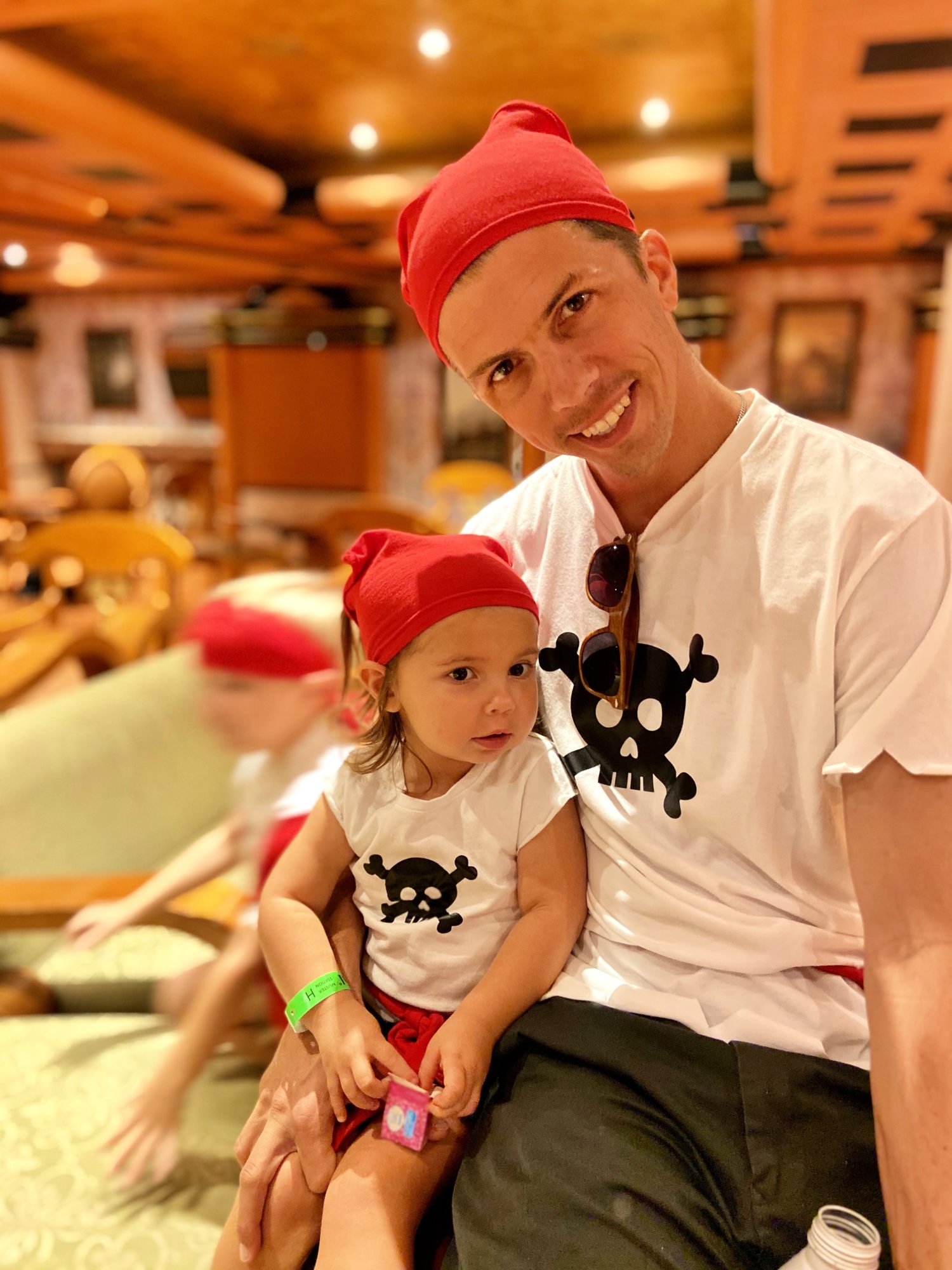 father and daughter dressed in pirate shirts with red do-rags on heads. 