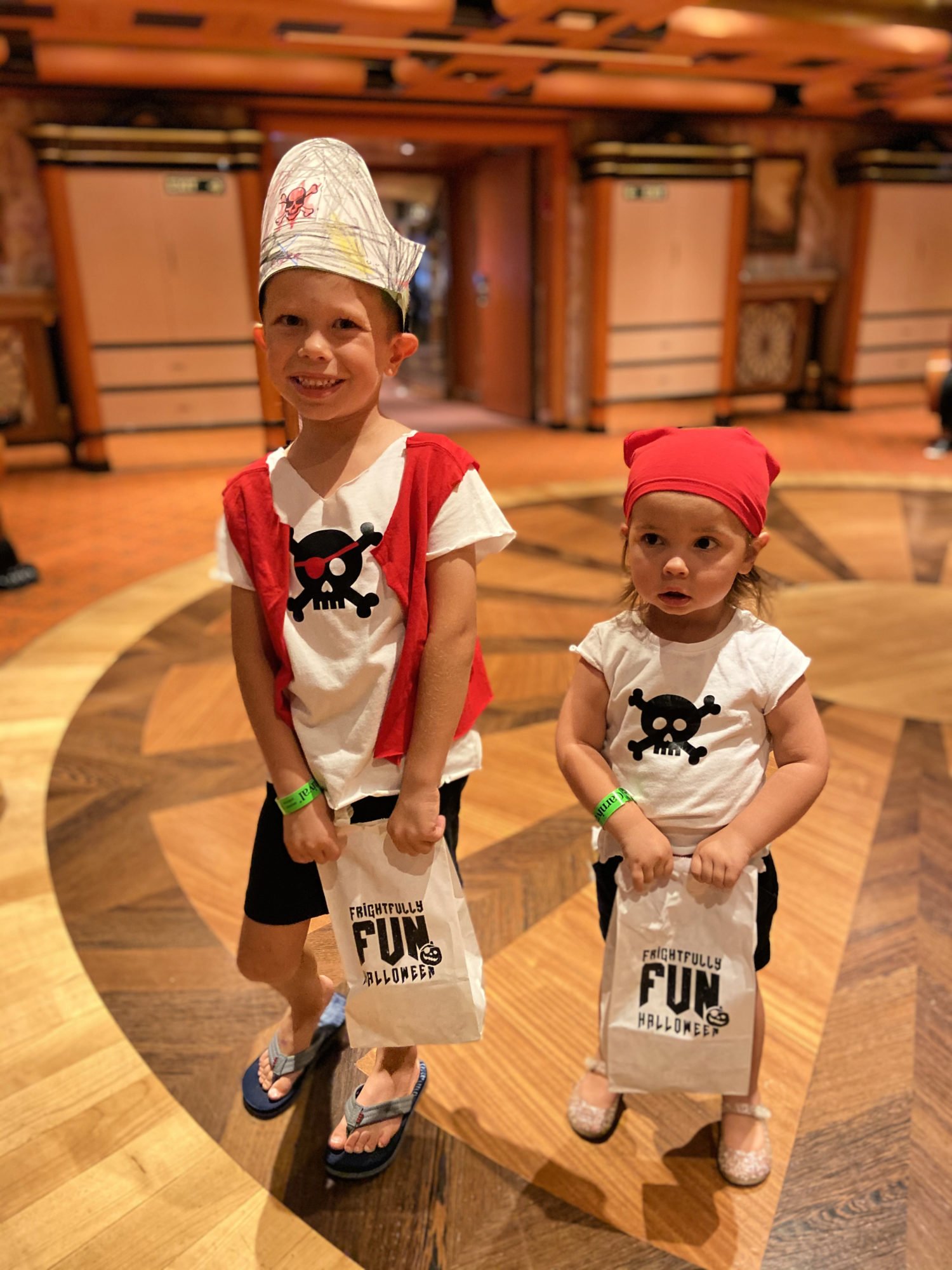 brother and sister dressed up with pirate shirts holding white paper bags. 