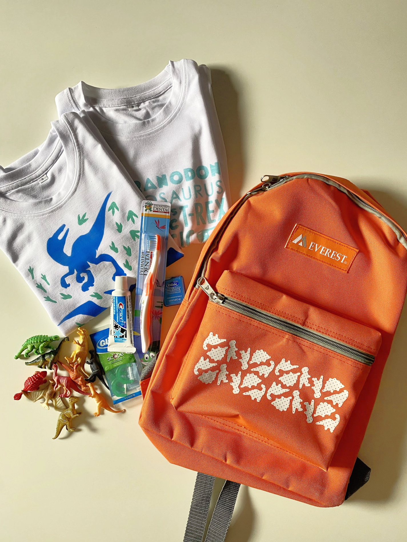 Orange Dinosaur Backpack with Dinosaur shirts, toys, and toothbrush. 