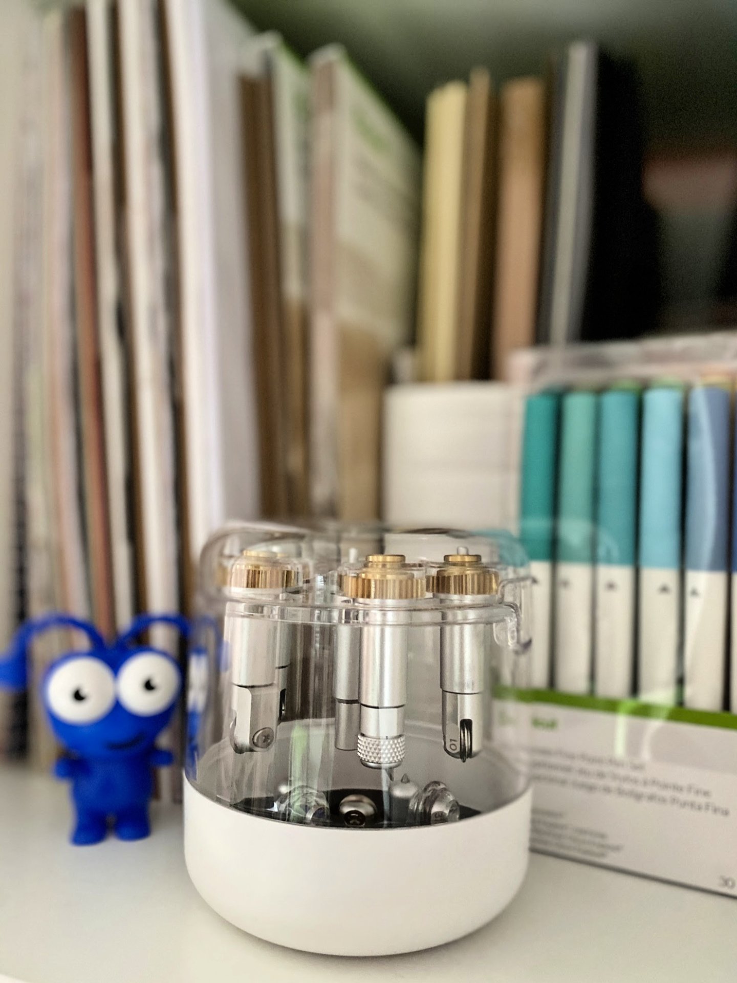 A close up of the Cricut Machine Tool Organizer on a craft room shelf with pens and a Cricut Cutie in the background.