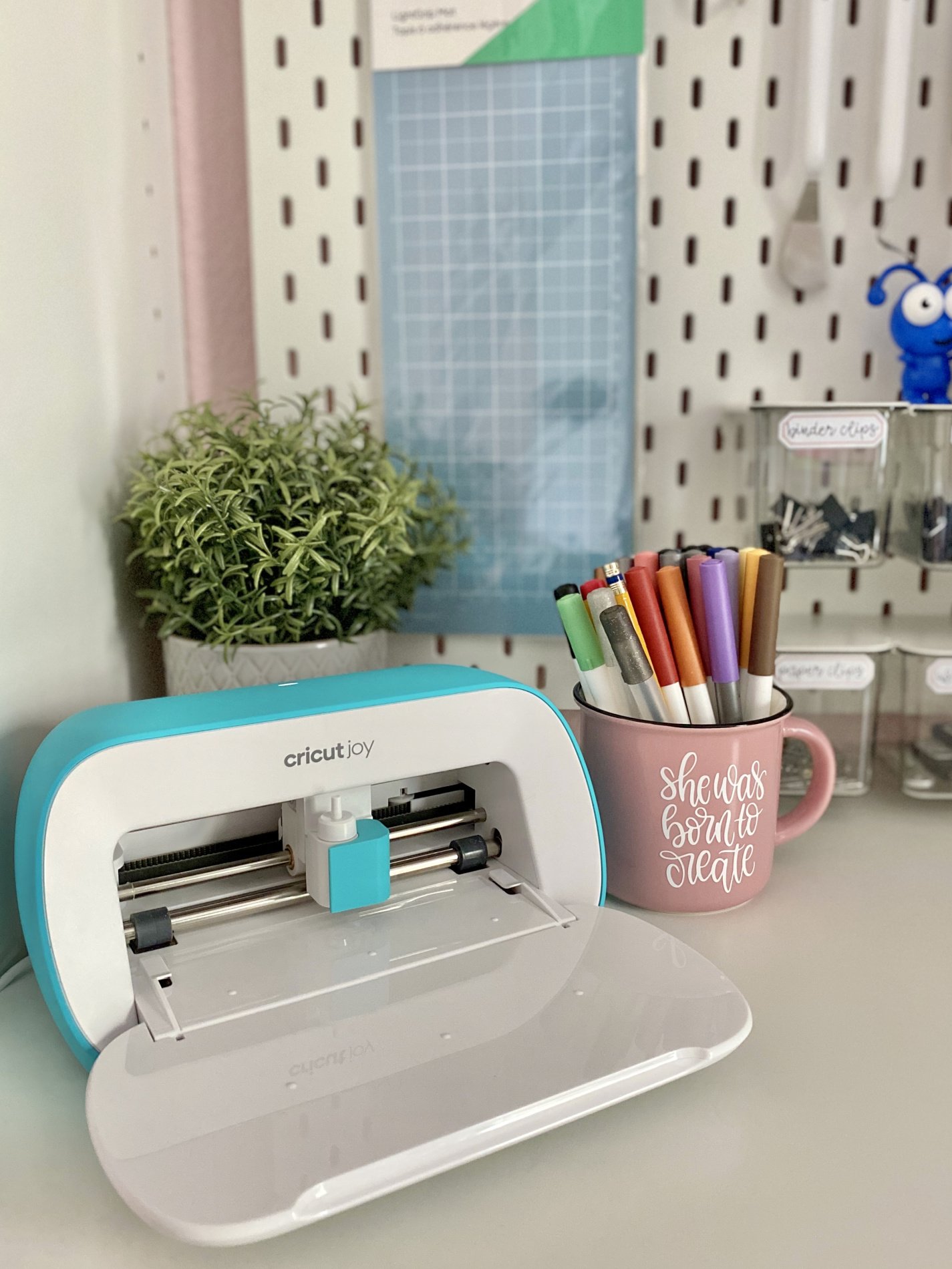 Cricut Joy with peg board in background with Cricut blue mat and pink cup.