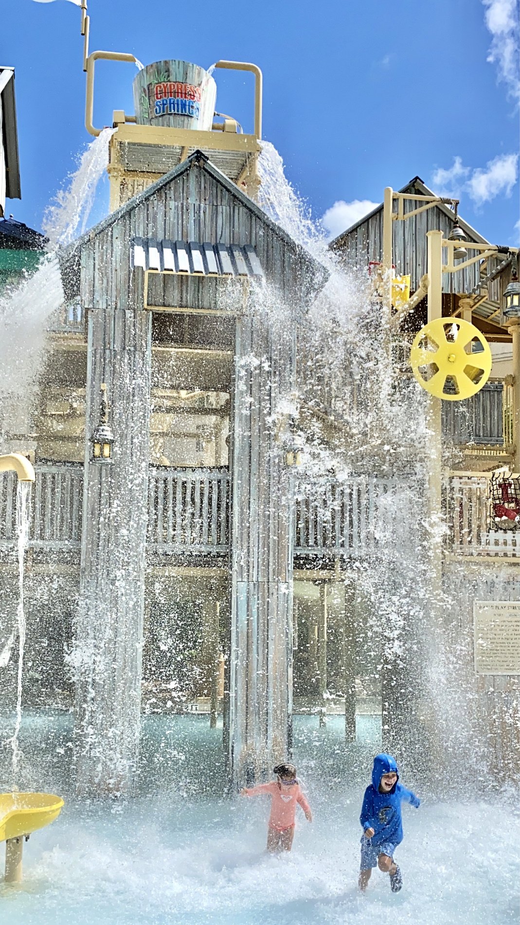 Two children running in a water park after water dumping on them. 