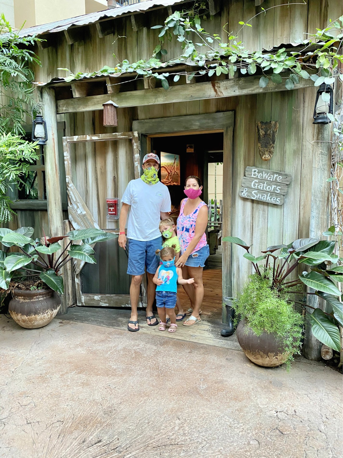 Family with mask on standing in front of house with plants.