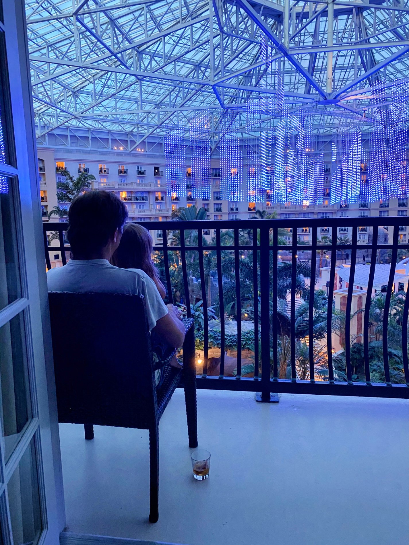 Child sitting on father's lap on balcony watching light show in hotel.