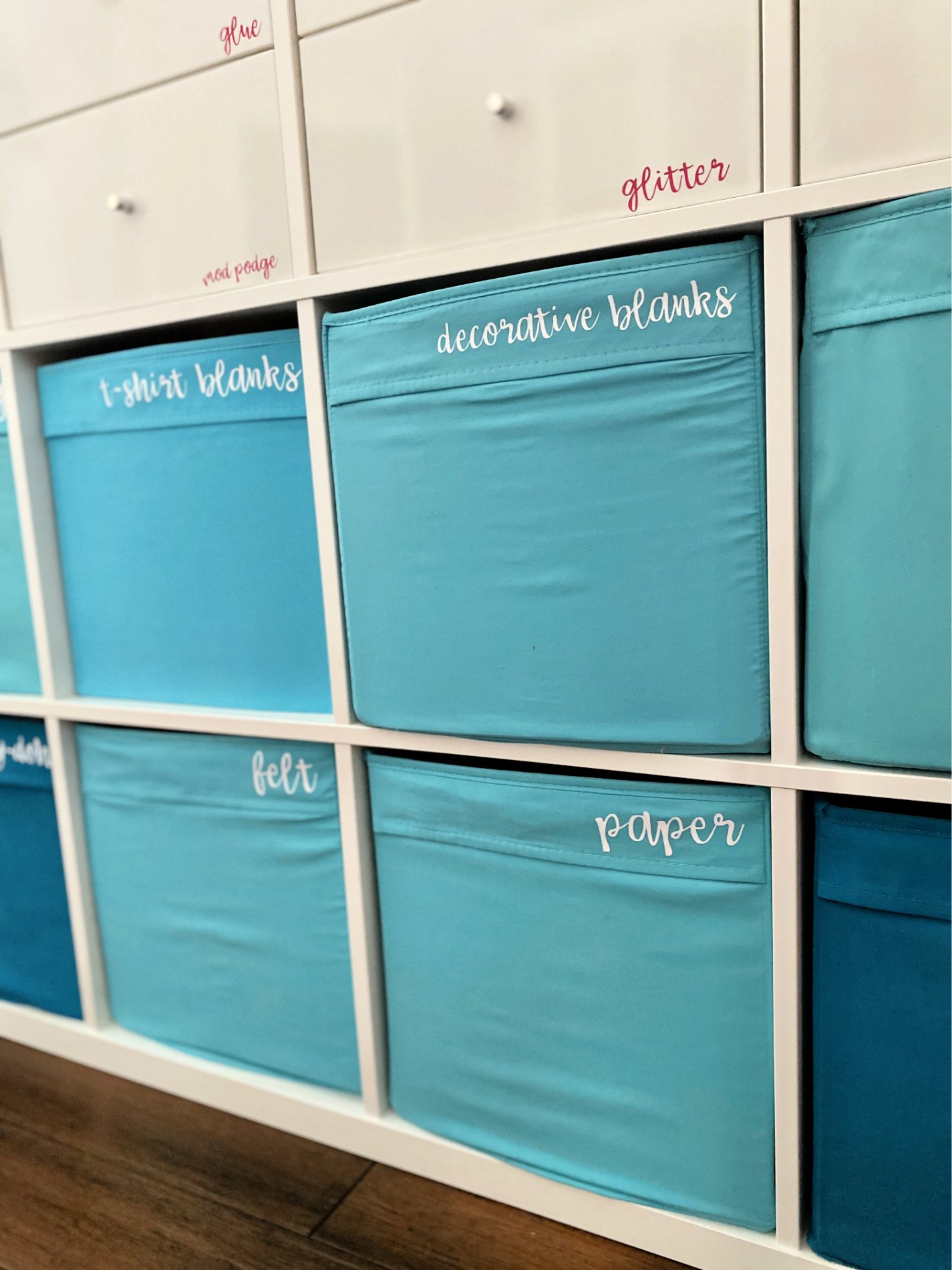 White cube shelve holding blue cloth bins with text on bins.