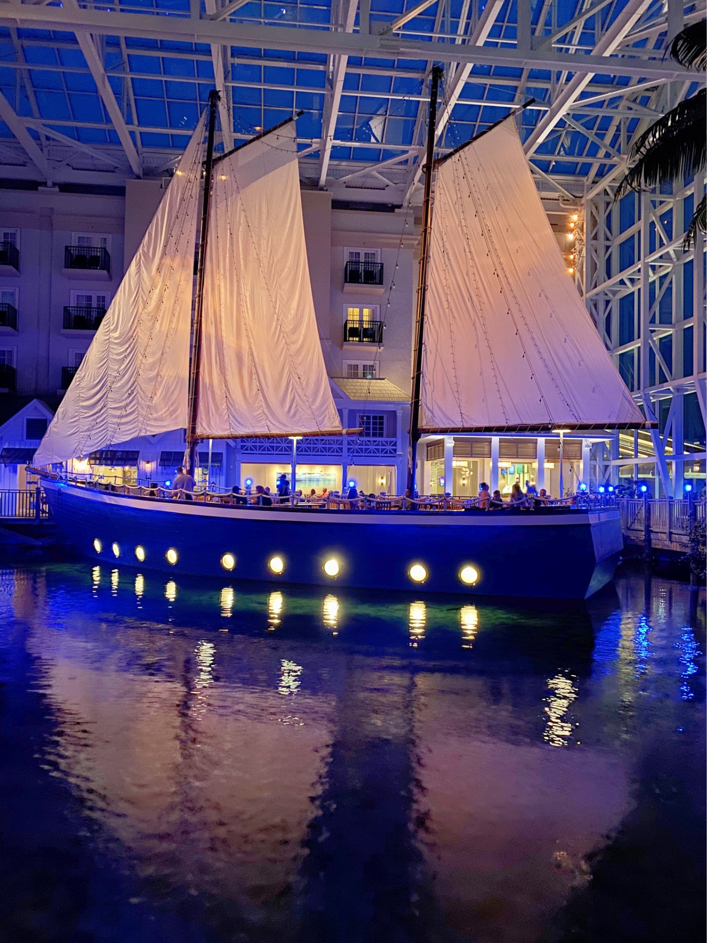 Boat on water in doors during the evening with people dining on the boat.