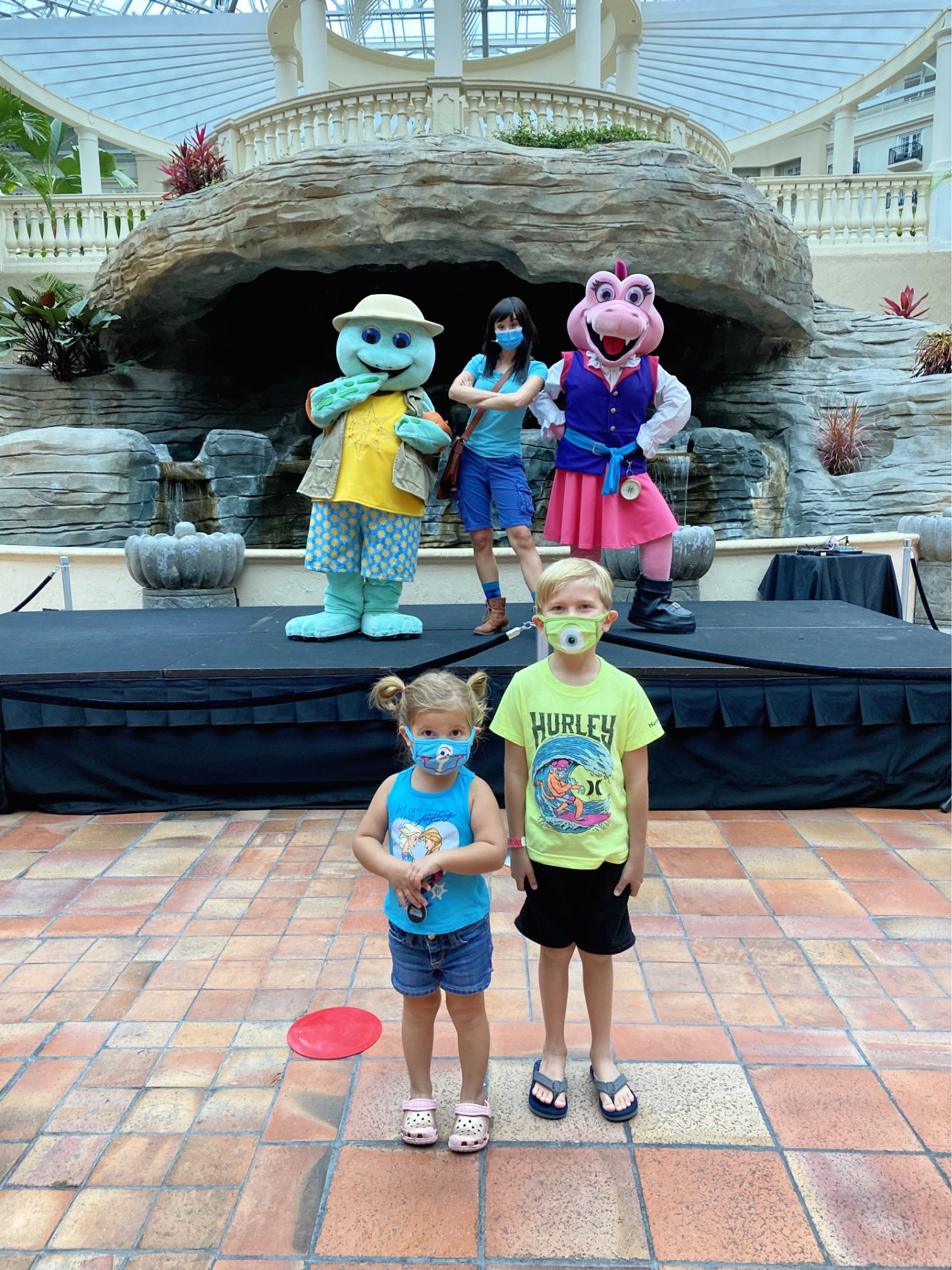 Boy and girl standing with mask with characters on stage behind them.