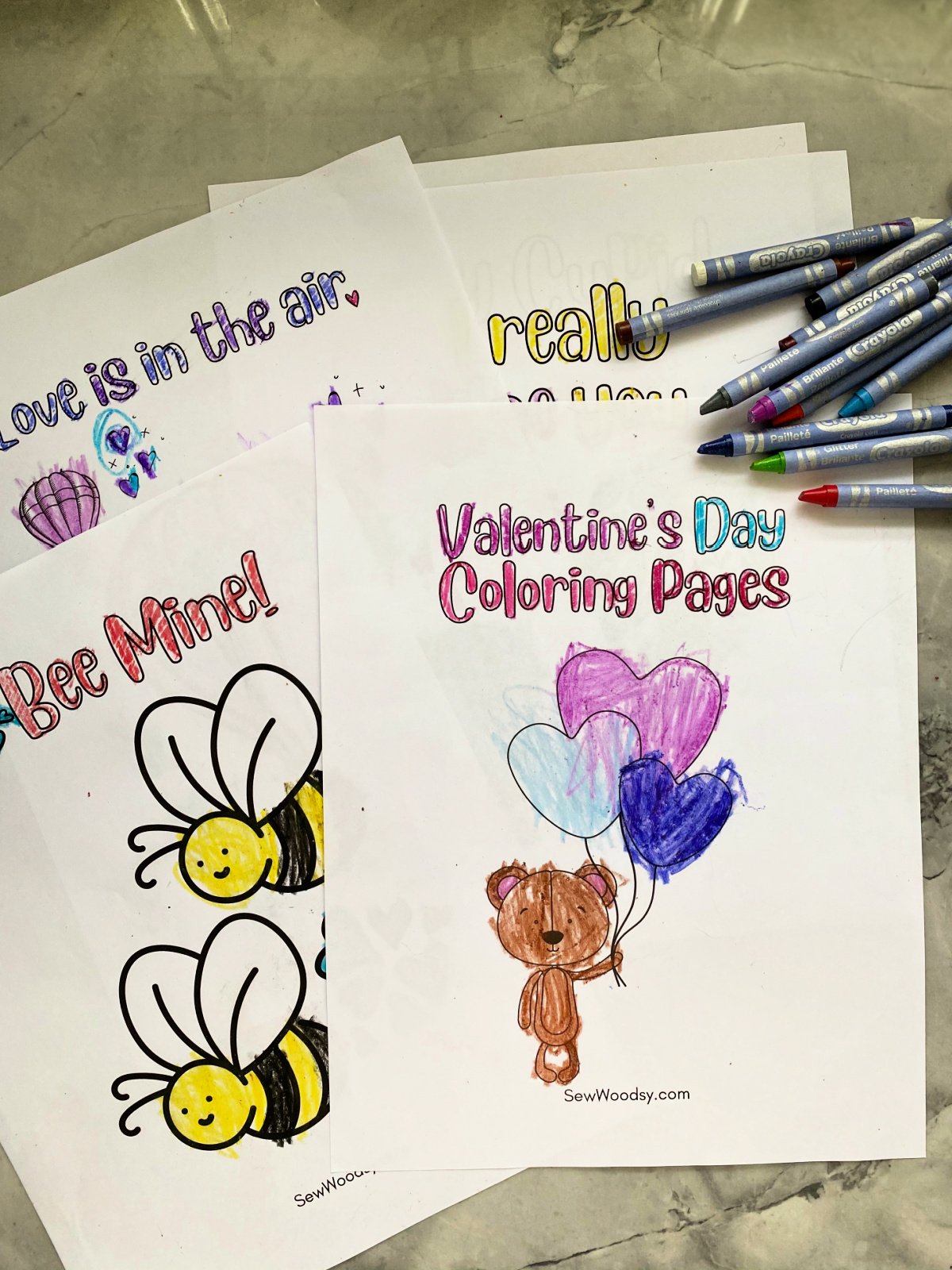 Five coloring sheets for Valentine's scattered with crayons on top.