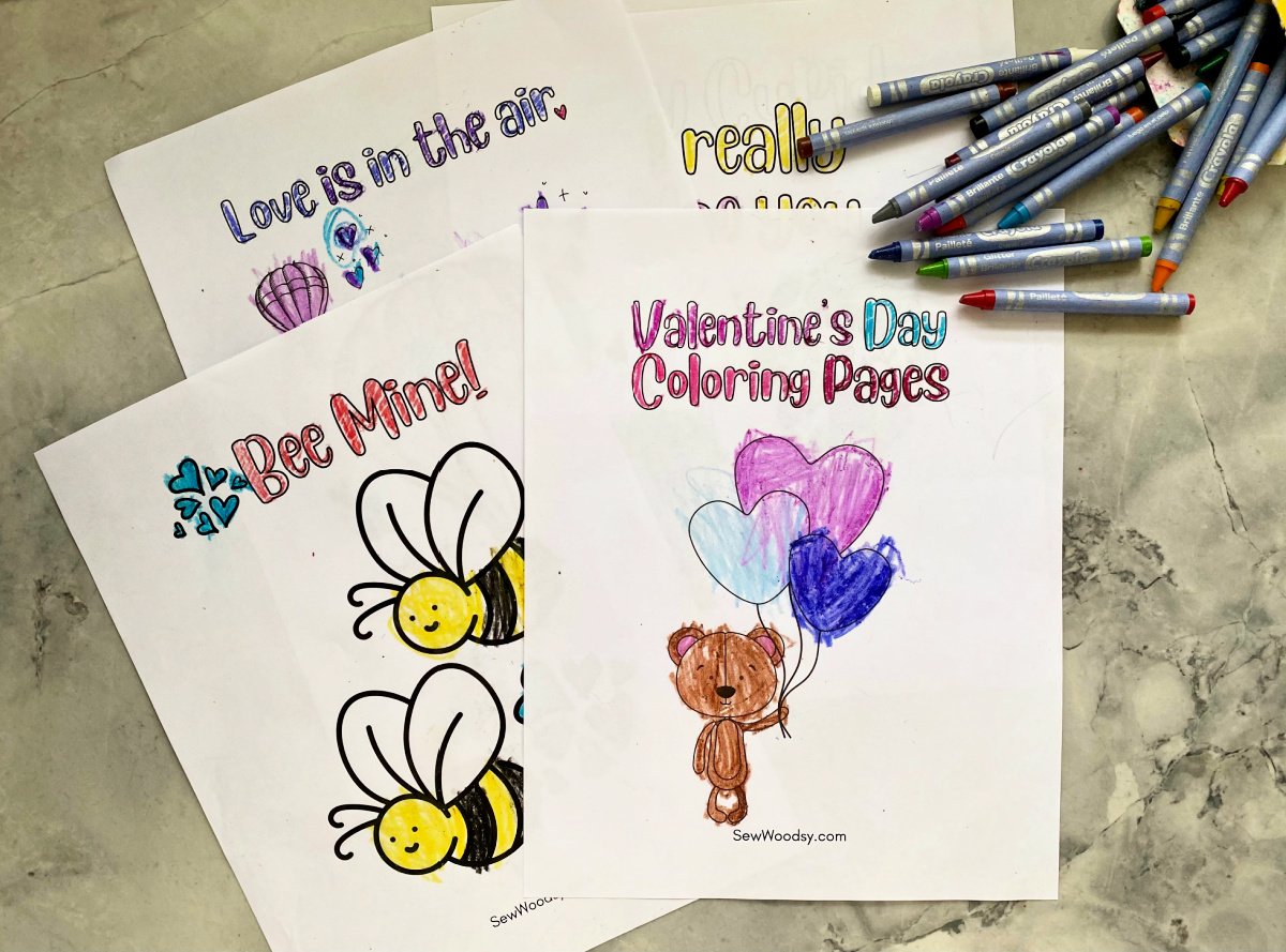 Top view of four coloring pages for kids on Valentine's Day with crayons scattered on top.