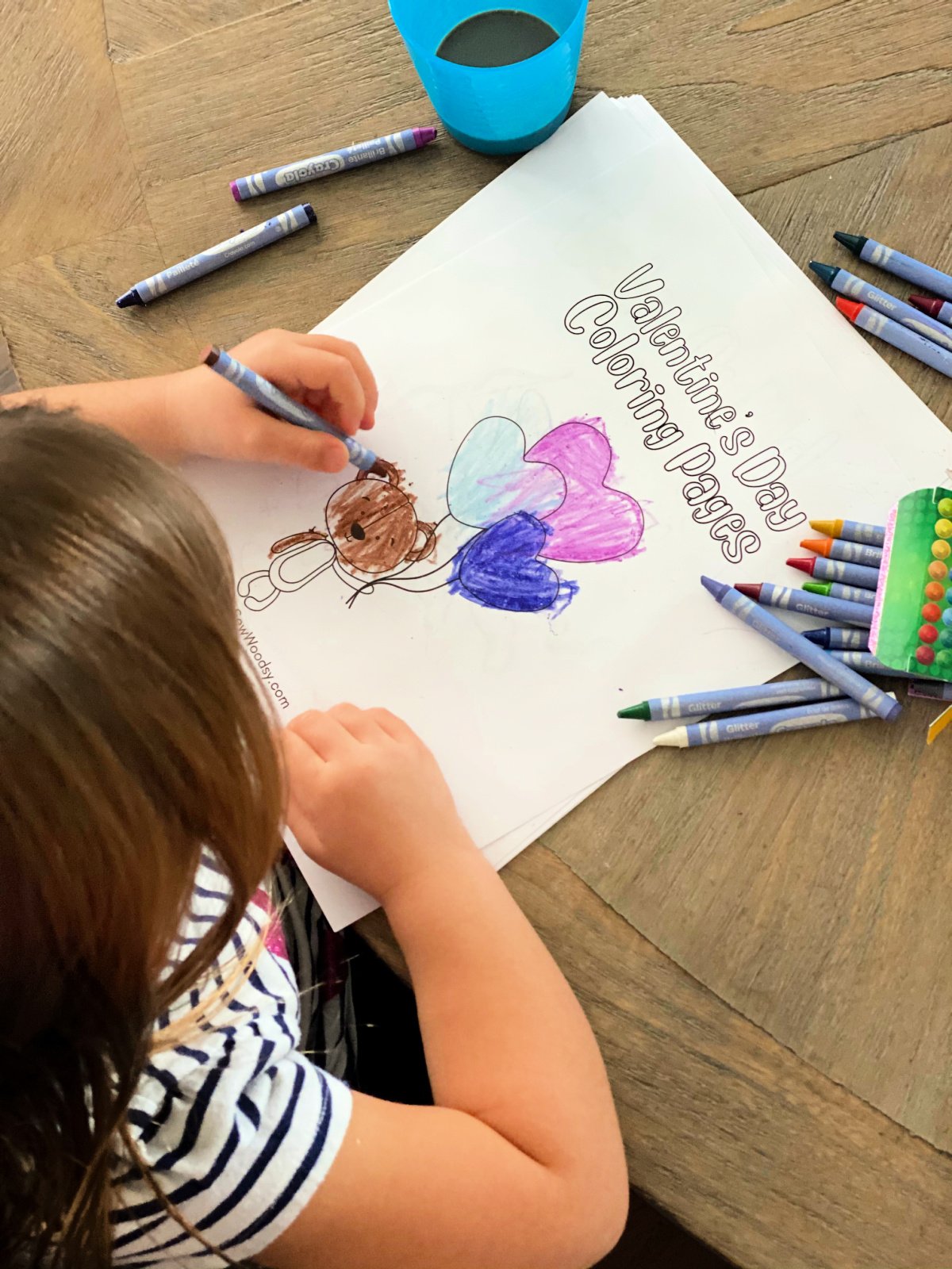 little girl coloring a bair brown holding balloons with crayons scattered on table.