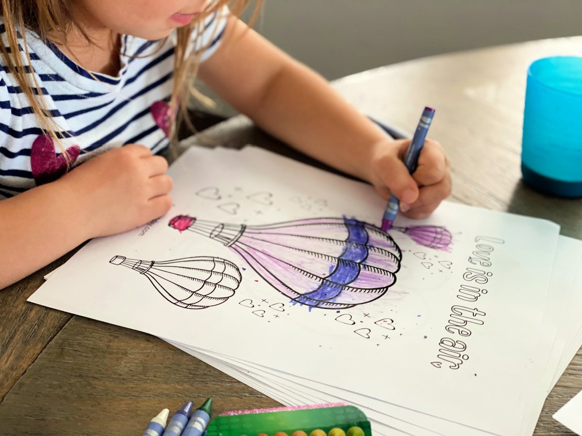 Close up of a little girl coloring hot air balloons with a purple crayon.